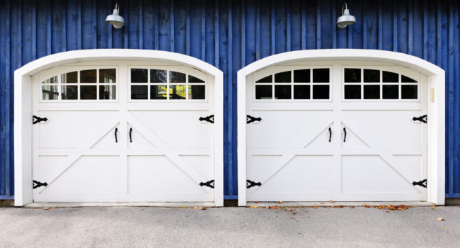 Two white garage doors with windows on blue house